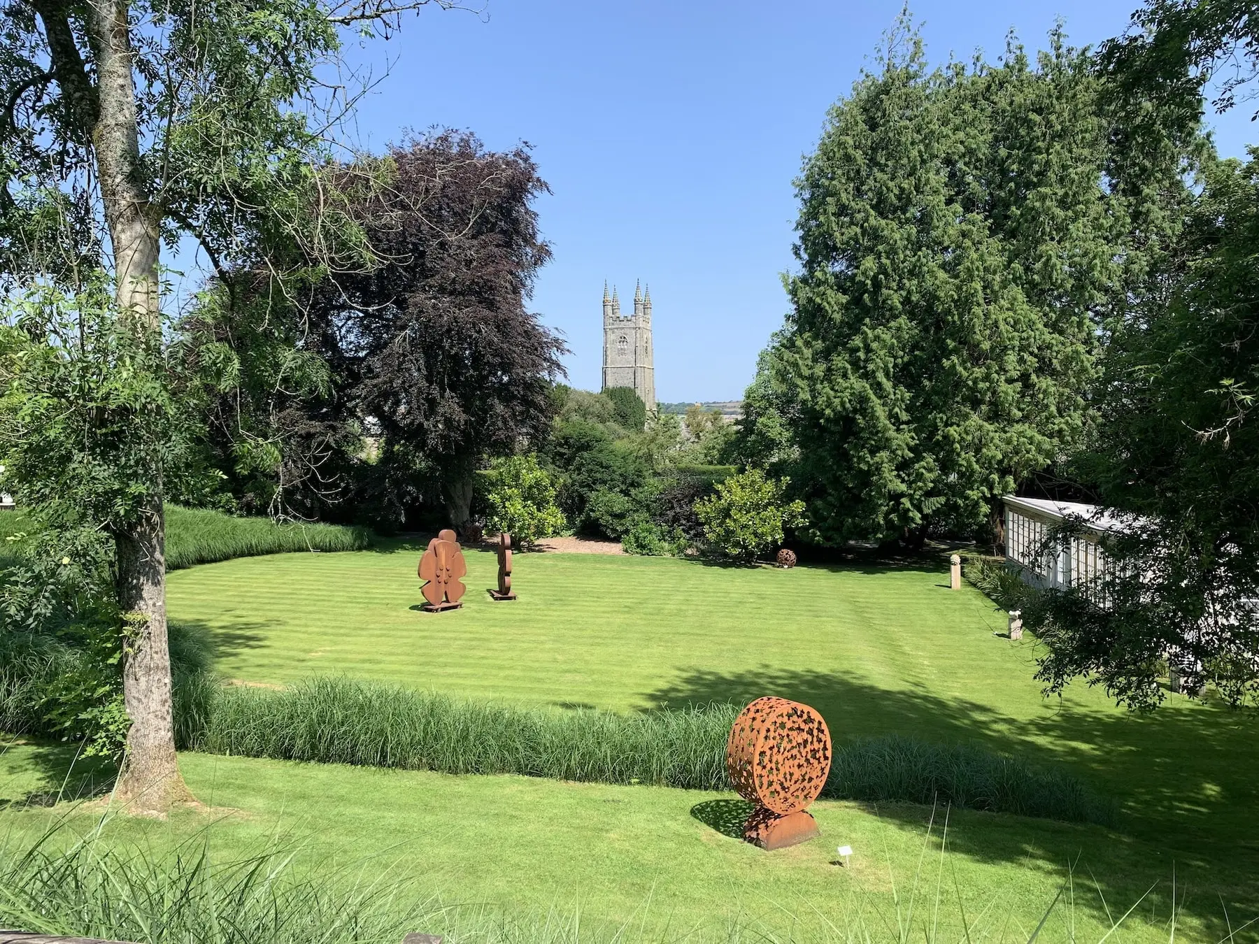 Withiel House garden with a maintained lawn, mature trees and church tower beyond